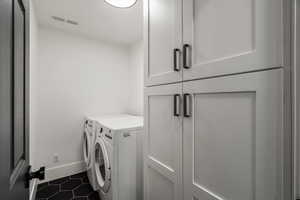 Laundry room with dark tile patterned flooring, washing machine and dryer, and cabinet space