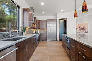 Kitchen featuring light stone countertops, dark wood finish cabinetry, high quality appliances, and hanging light fixtures