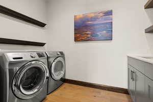 Laundry area featuring light wood-style floors, washer and clothes dryer, and cabinet space
