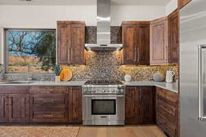 Kitchen featuring premium appliances, backsplash, dark wood finish cabinetry, light wood finished floors, and light stone counters