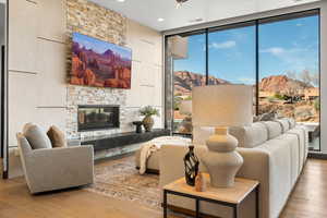 Living area featuring light wood-type flooring, a stone fireplace, and expansive windows