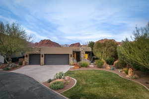 Pueblo-style home featuring a garage, stucco siding, a mountain view, concrete driveway, and a front yard