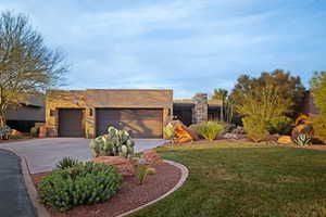 View of front of house with a front yard, a garage, stone siding, driveway, and stucco siding