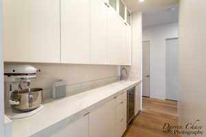 Kitchen featuring modern cabinets, glass fronted cabinets, white cabinetry, light wood-style floors, and light stone counters