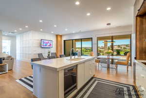 Kitchen featuring open floor plan, light wood-style floors, decorative light fixtures, light stone counters, and white cabinetry