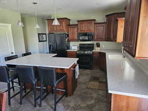 Kitchen featuring black appliances, a kitchen bar, a kitchen island, dark stone finish flooring, and hanging light fixtures