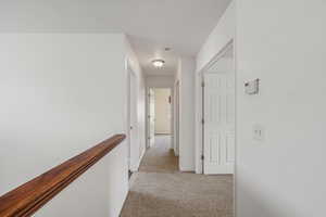 Corridor featuring light colored carpet and an upstairs landing