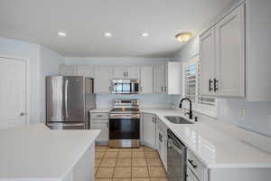 Kitchen with stainless steel appliances, recessed lighting, light stone counters, light tile patterned flooring, and white cabinetry