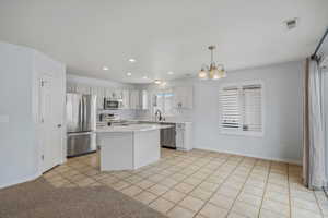 Kitchen featuring light tile patterned floors, stainless steel appliances, a chandelier, a kitchen island, and white cabinets