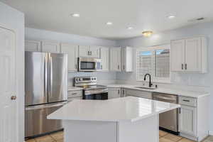 Kitchen with stainless steel appliances, light stone countertops, white cabinetry, recessed lighting, and a center island