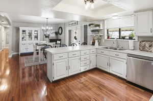 Kitchen featuring a peninsula, light countertops, white cabinets, stainless steel dishwasher, and dark wood finished floors