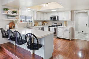 Kitchen featuring a breakfast bar, a peninsula, light countertops, stainless steel appliances, and white cabinetry