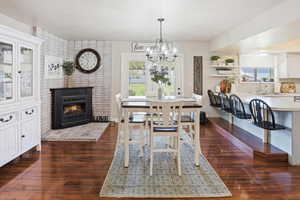 Dining area with a brick fireplace, dark wood finished floors, and hanging lights