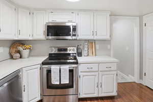 Kitchen with stainless steel appliances, light countertops, white cabinets, and dark wood finished floors