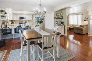 Dining space featuring dark wood-style flooring, a chandelier, and arched walkways