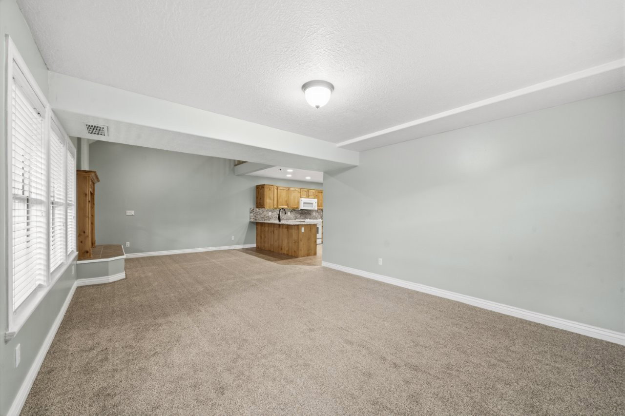 Unfurnished living room featuring light carpet, bar with sink, and a textured ceiling