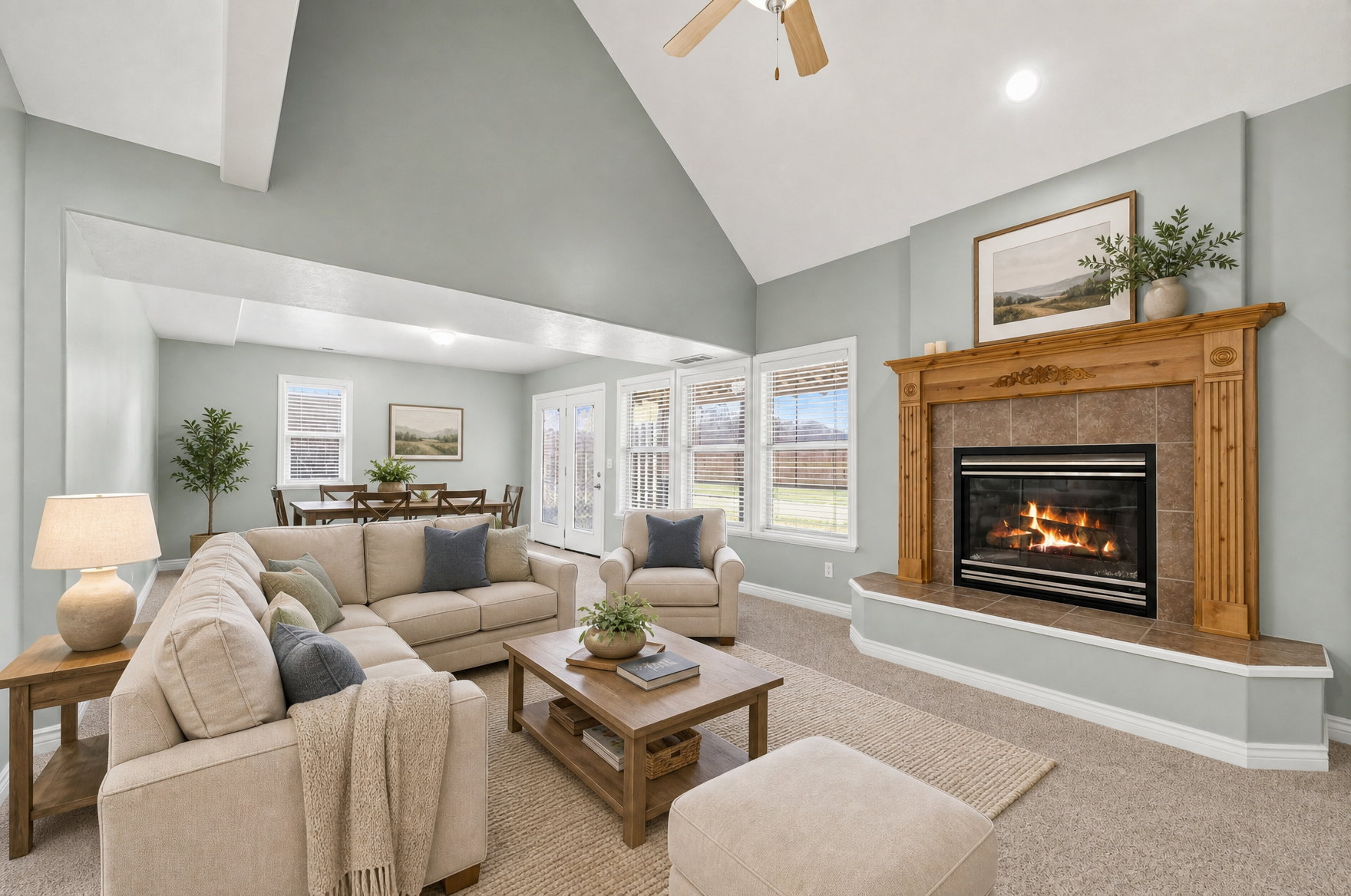 Vaulted ceiling living area featuring a central fireplace with a wood mantel and tile surround, multiple windows, and light-colored carpeting