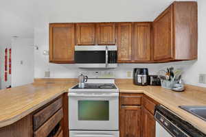 Kitchen with white appliances, light countertops, wood finish cabinets, and a peninsula