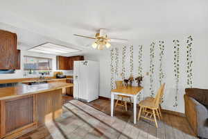 Kitchen featuring wood finish cabinetry, white refrigerator with ice dispenser, light countertops, ceiling fan, and a peninsula