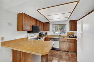 Kitchen with a peninsula, light countertops, white appliances, wood finish cabinetry, and stone finish floors