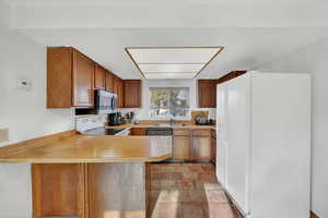 Kitchen with a peninsula, wood finish cabinetry, white appliances, and light countertops