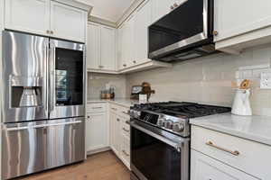 Kitchen with stainless steel appliances, white cabinetry, light stone counters, backsplash, and light wood-style flooring