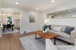 Living room with ornamental molding, arched walkways, wood-type flooring, and a chandelier