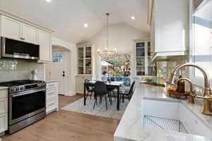 Kitchen featuring stainless steel appliances, decorative backsplash, light stone countertops, lofted ceiling, and glass insert cabinets
