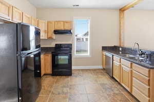 Kitchen with black appliances, light wood finish cabinets, dark stone counters, and a peninsula