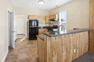 Kitchen with a peninsula, a breakfast bar area, black appliances, light wood finish cabinetry, and dark stone countertops