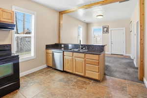 Kitchen with light wood finish cabinets, black / electric stove, a peninsula, stainless steel dishwasher, and exhaust hood