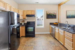 Kitchen featuring light wood finish cabinets, black appliances, and dark stone counters