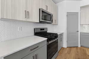 Kitchen featuring backsplash, stainless steel appliances, gray cabinets, light wood-style flooring, and light stone counters