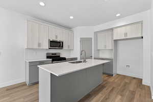 Kitchen with backsplash, stainless steel appliances, light stone counters, two tone color scheme, and light wood-type flooring