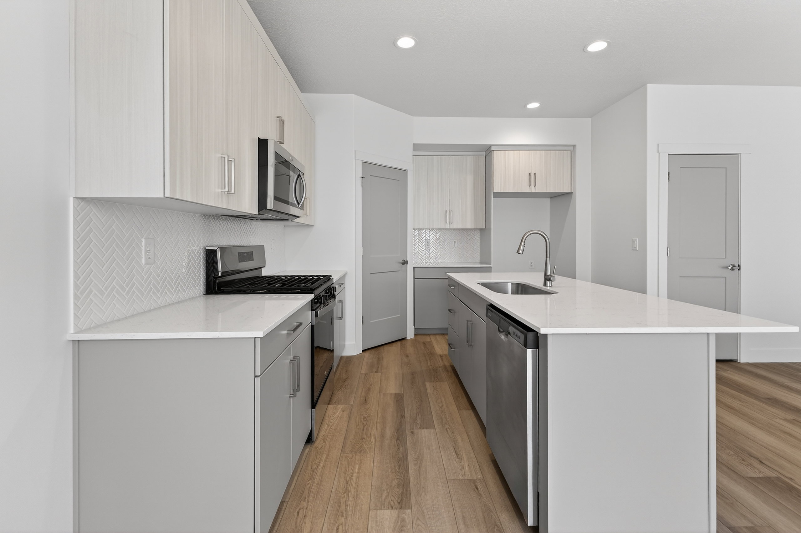 Kitchen with light stone countertops, stainless steel appliances, light wood-style flooring, a center island with sink, and dual tone cabinets