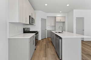 Kitchen with light stone countertops, stainless steel appliances, light wood-style flooring, a center island with sink, and dual tone cabinets