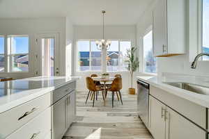 Kitchen with white cabinetry, light stone counters, light wood-style floors, stainless steel dishwasher, and suspended lighting