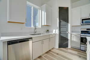 Kitchen with stainless steel appliances, white cabinets, light stone countertops, and light wood finished floors