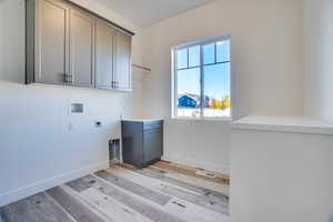 Laundry area featuring hookup for a washing machine, electric dryer hookup, cabinet space, and light wood finished floors