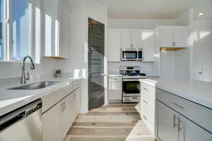 Kitchen featuring stainless steel appliances, light stone counters, white cabinetry, and light wood-style flooring
