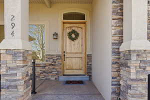 Entrance to property featuring stone siding, stucco siding, and covered porch