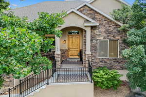 View of exterior entry featuring stucco siding, roof with shingles, and stone siding