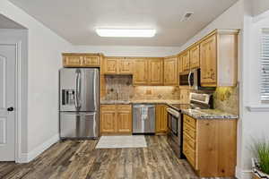 Kitchen with stainless steel appliances, light stone counters, dark wood-style flooring, and tasteful backsplash
