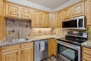 Kitchen with stainless steel appliances, tasteful backsplash, light stone countertops, and light wood finish cabinets