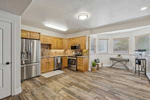Kitchen featuring stainless steel appliances, decorative backsplash, light wood-style flooring, light stone counters, and light wood finish cabinets