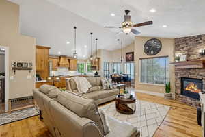 Living room featuring ceiling fan, light wood-style flooring, a stone fireplace, vaulted ceiling, and recessed lighting