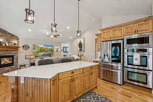 Kitchen featuring vaulted ceiling, stainless steel appliances, a center island, wood finish cabinets, and open floor plan