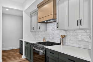 Kitchen with gas range oven, light wood-type flooring, light stone counters, tasteful backsplash, and two tone cabinetry