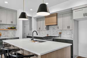 Two tone kitchen featuring two tone cabinets, light stone countertops, a kitchen island with sink, stainless steel range with gas cooktop, and a kitchen breakfast bar