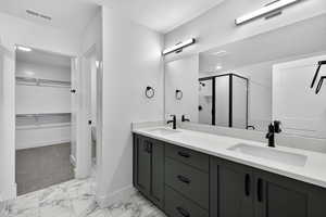 Bathroom featuring a spacious closet, double vanity, a shower stall, a textured ceiling, and light marble finish floors
